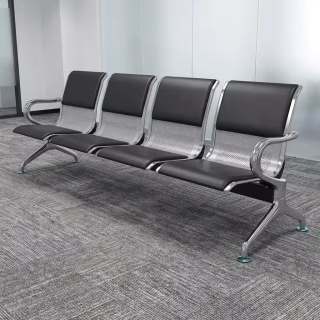 Four-seater commercial public waiting bench with a perforated stainless steel frame, polished chrome armrests and legs, and integrated black faux leather padded seat and back cushions.